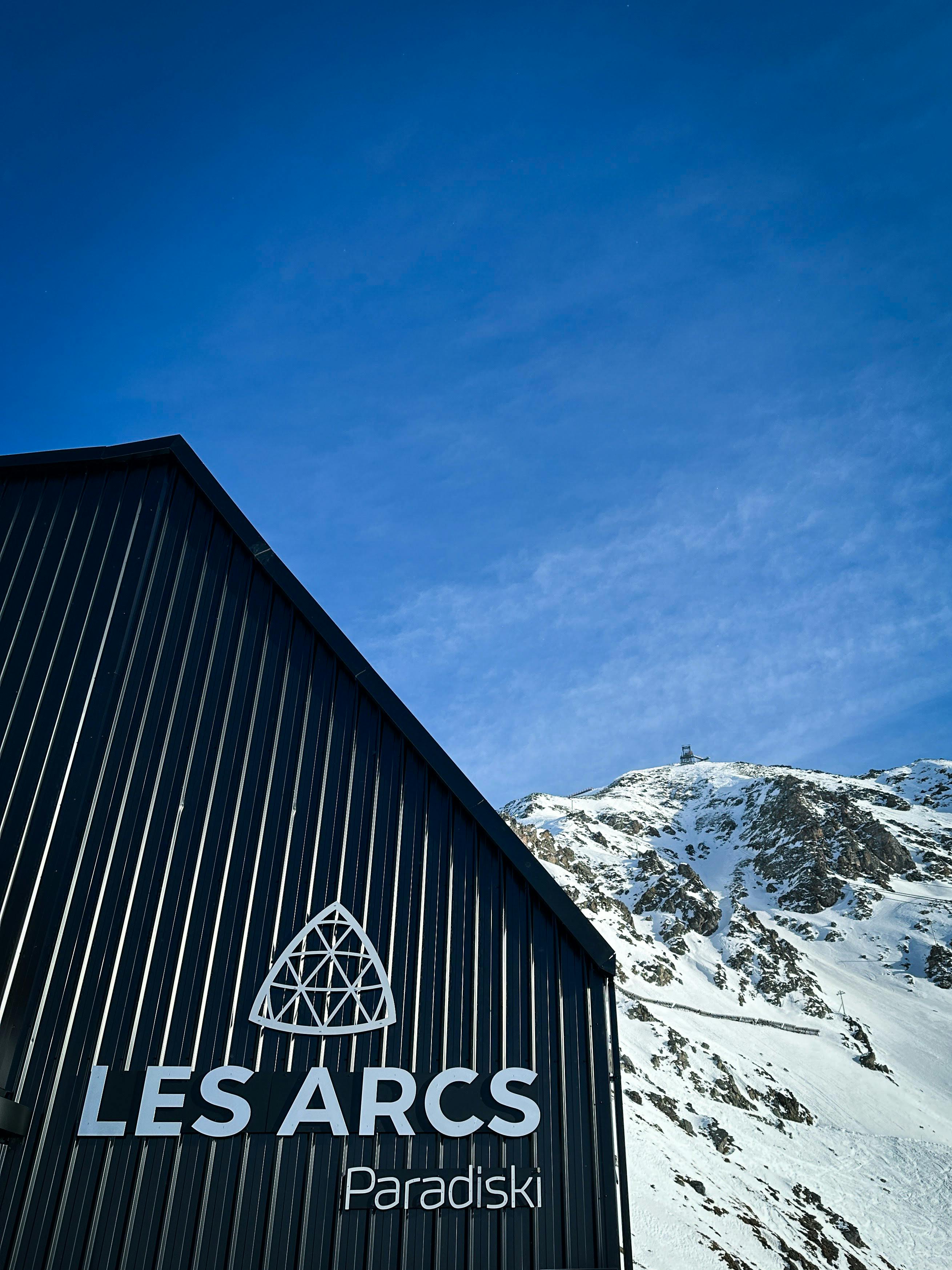 Les Arcs Paradiski ski area sign on a mountainside building with snowy peaks behind in the French Alps